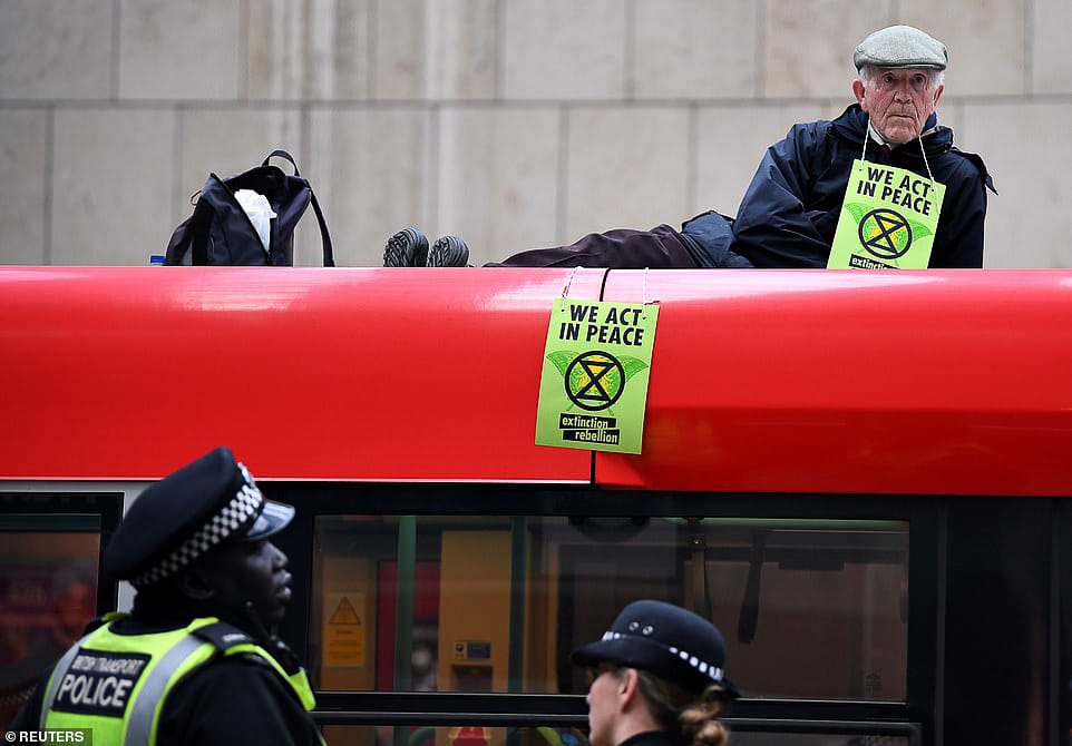 An XR protester glued to the roof of a Docklands Light Railway train, with the XR logo prominently displayed