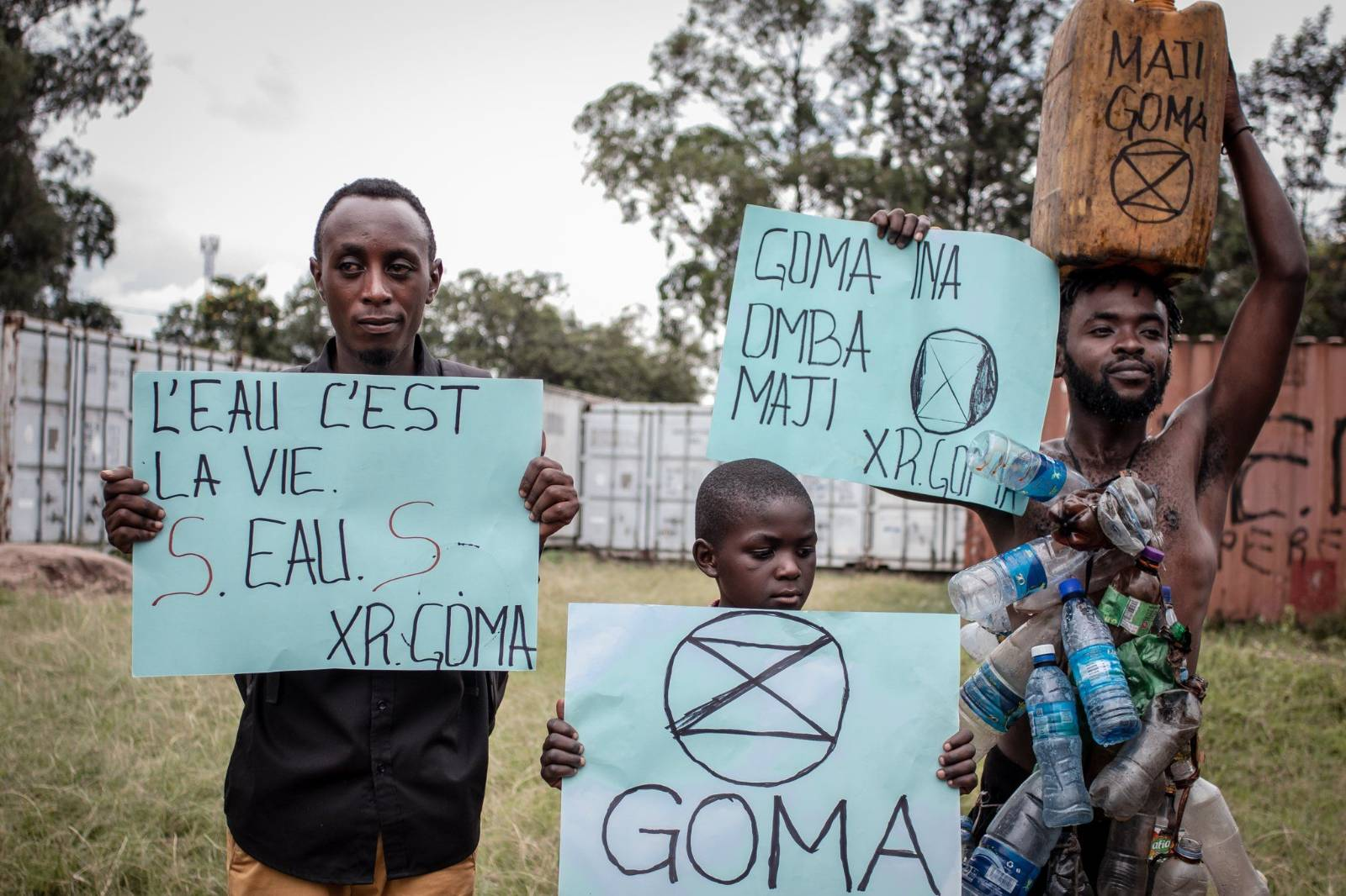 Three people from XR Goma, DRC, holding hand-made XR protest signs